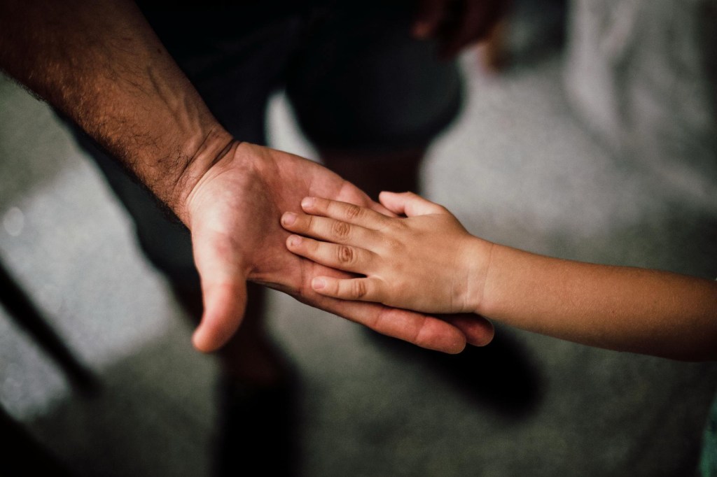 A close-up image of an adult hand and a child's hand touching, symbolizing connection and affection.