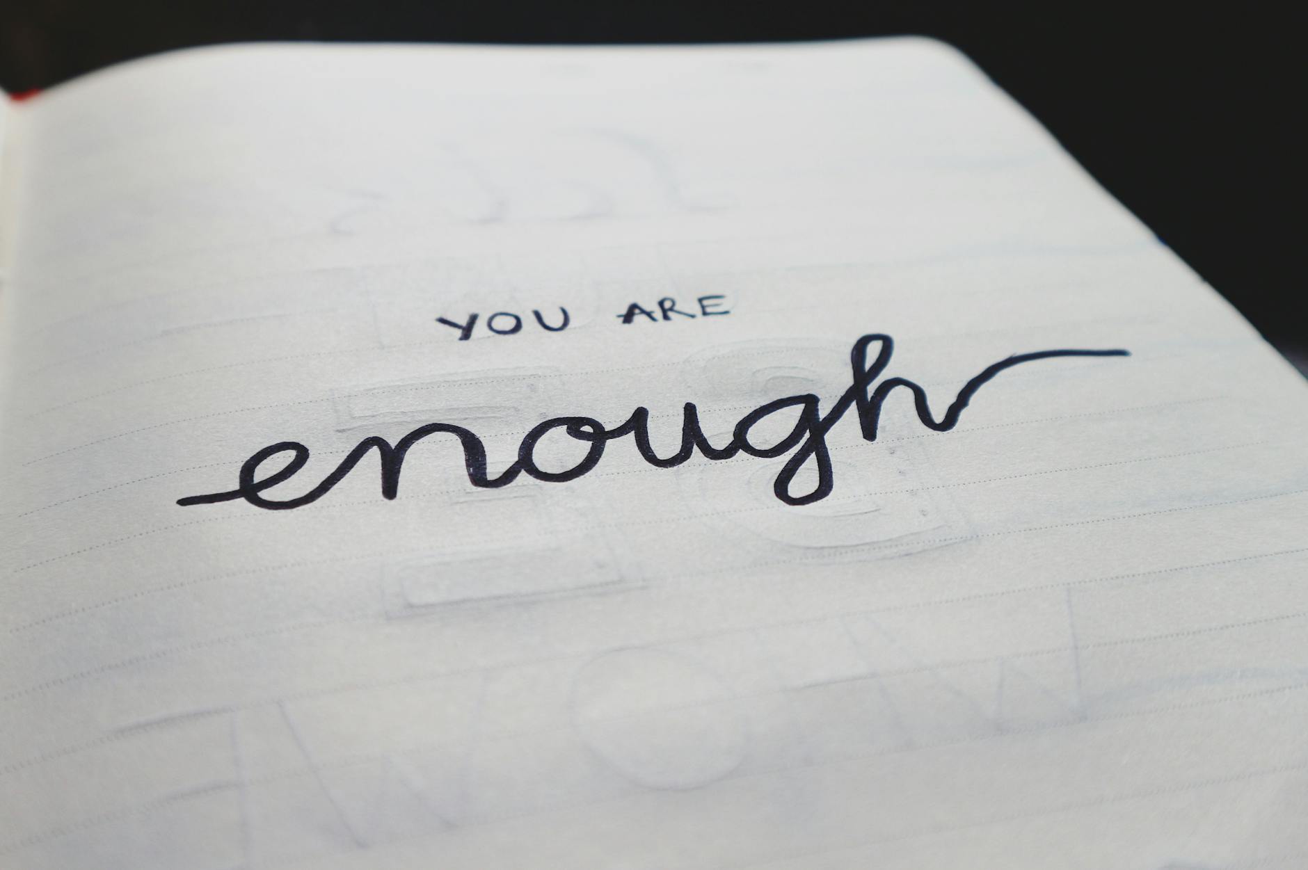 A close-up of a handwritten note that says 'You are enough' on a lined notebook page.