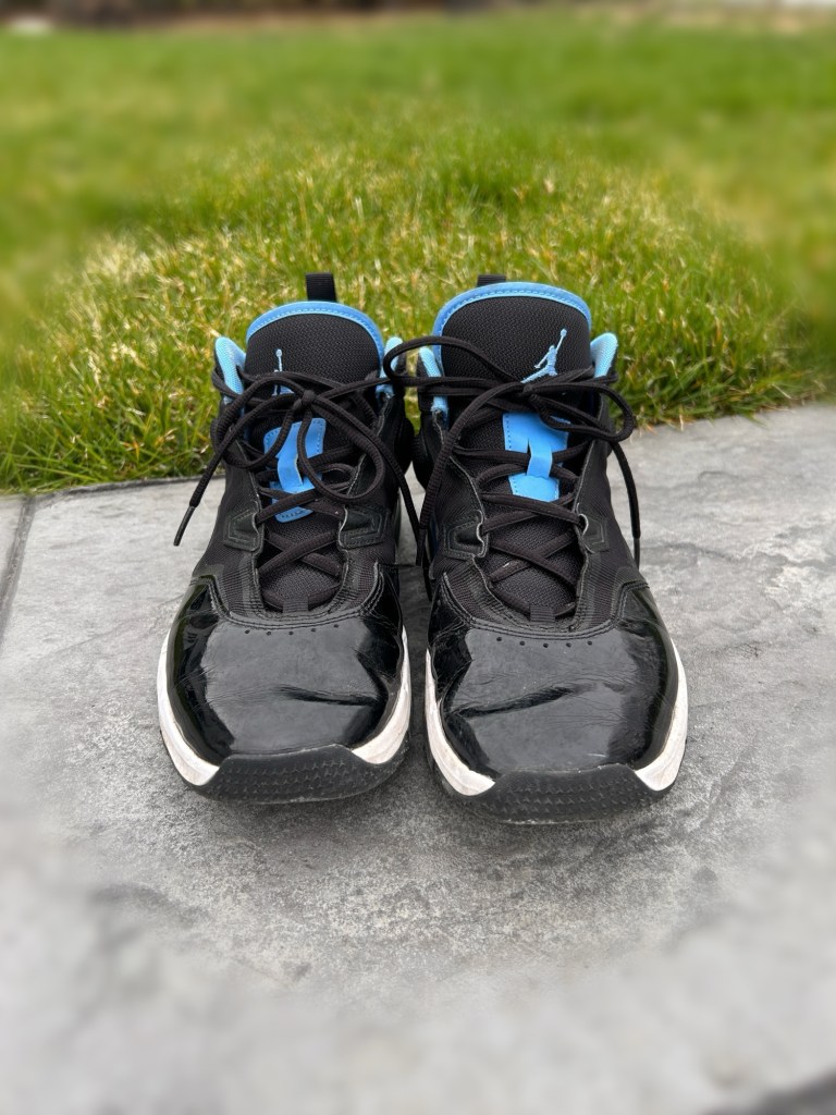 A pair of black and blue basketball shoes placed on a stone surface with green grass in the background.